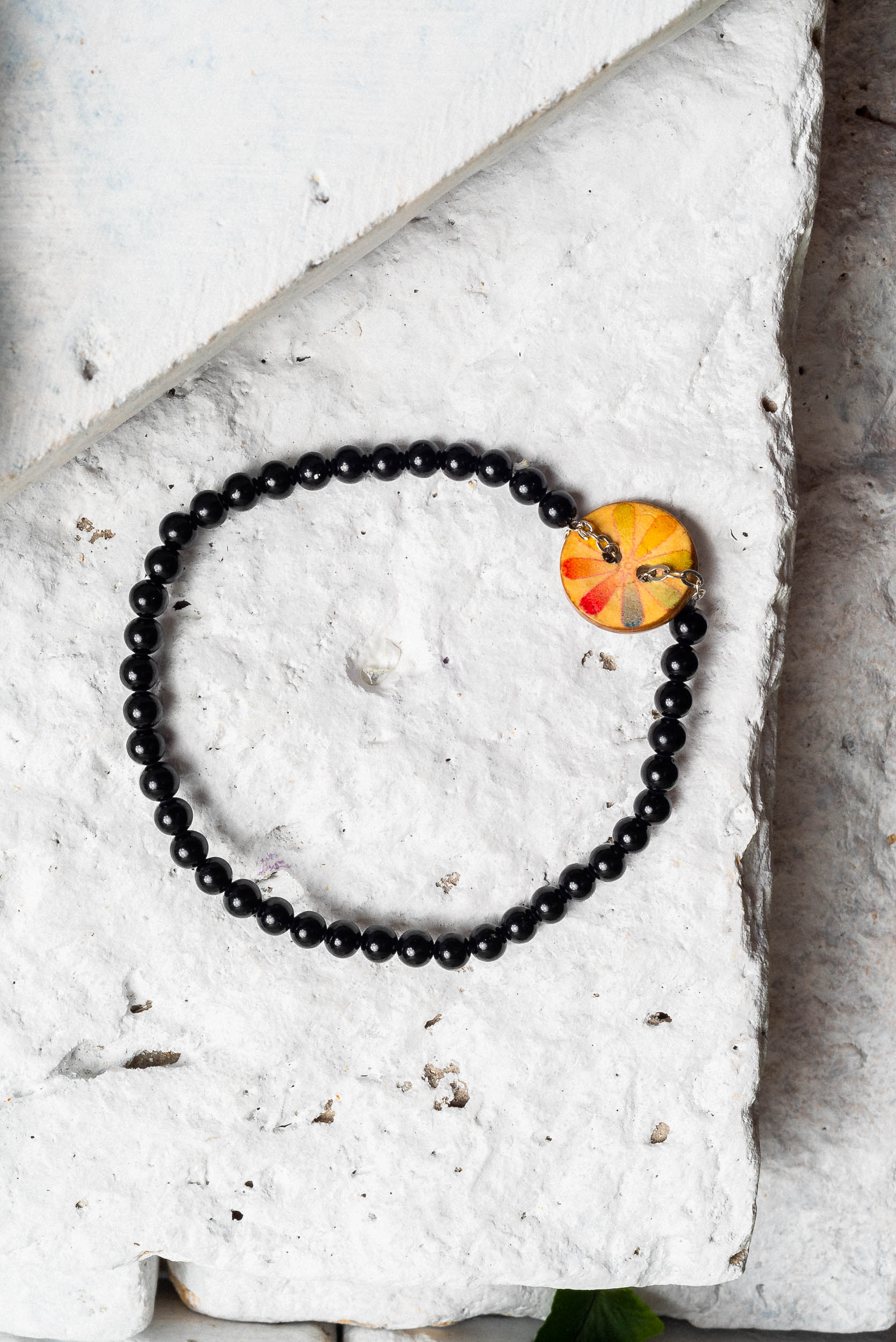 coconut shell bracelet with small black beads and a coconut shell charm with a subtle rainbow flower painted on it